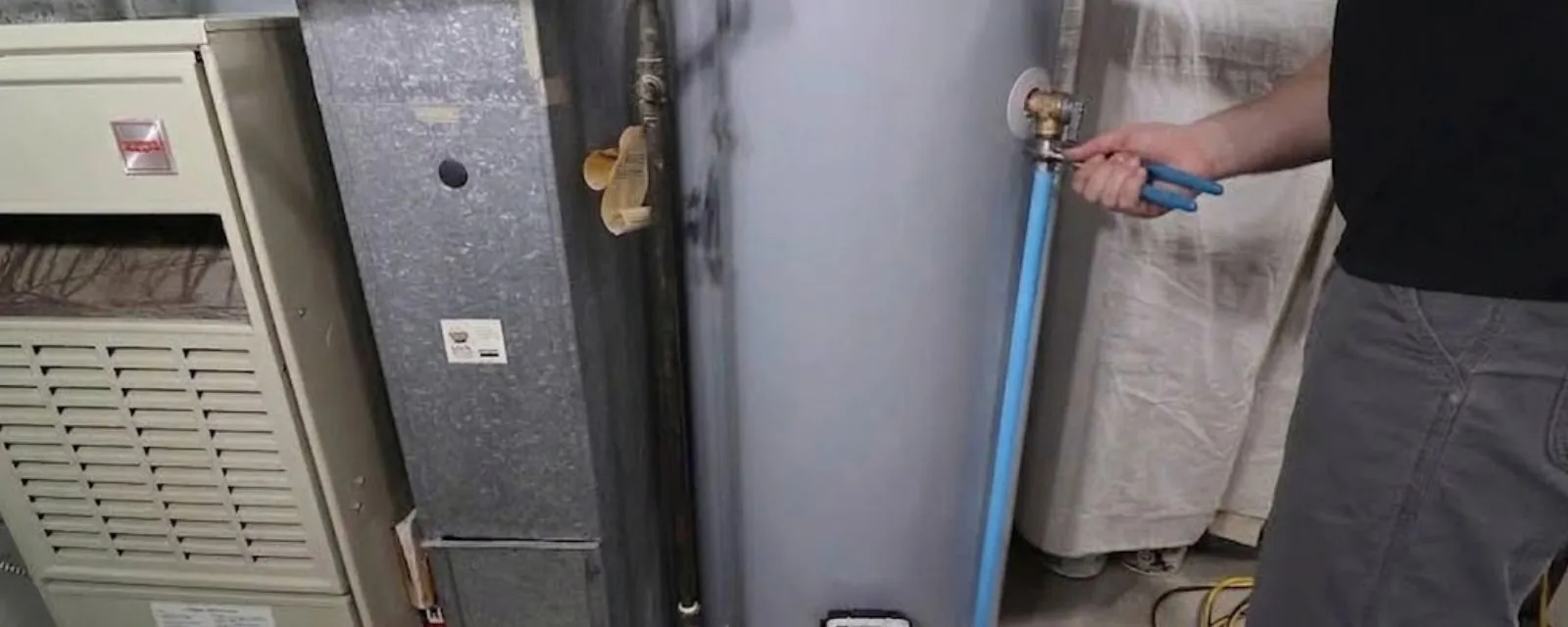 Hands connecting a water line to a tank water heater installed next to a furnace